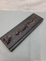 Top view of rectangular wooden box showing fish and frog carvings on lid with carved leaf and floral patterns.