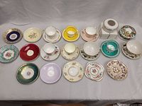 Group photo of vintage tea cups and saucers with mixed floral and gold patterns, assorted colors including red, blue, yellow, lavender, teal, and white with gold trims