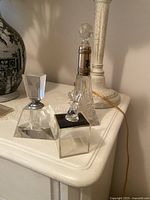 Photo of two vintage glass perfume bottles and small acrylic trinket box with rabbit figure on top, arranged on a white surface.