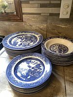 Three stacks of Blue Willow dinnerware on countertop: dinner plates, soup bowls, lunch plates