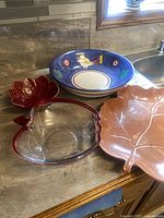 Photo showing blue ceramic bowl with bird design, large pink ceramic leaf dish, red glass apple bowl, and two small red ceramic leaf dishes on kitchen counter