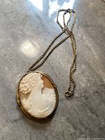 Overall view of the antique shell cameo necklace with chain laid flat on surface.
