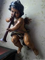 Front three-quarter view of wood angel cherub mounted on wall, holding trumpet