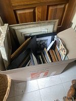 Box filled with assorted picture frames and prints, showing variety of sizes and materials