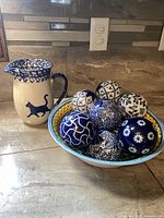 Image showing white ceramic pitcher with blue cat silhouette and spongeware pattern next to a plastic bowl filled with decorative ceramic balls.