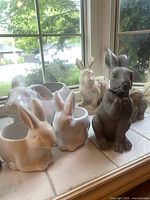 Photo showing three white ceramic rabbit planters with glossy finish in different poses: lying down, sitting upright, and a smaller one.