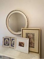 Photo of entire lot showing round mirror, paired floral prints, cherub painting, and floral sketch print.