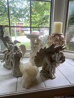 Wide view of six angel figurines and decorative pieces on tiled surface by window, showing variety in style and material for lot description and condition assessment