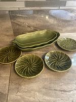 Overall view of the 6 olive green ceramic serving dishes including 4 round plates and 2 larger leaf-shaped dishes.