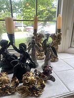 Overview showing 3 pairs of candle holders and cherub wall decor on window tile with daylight background.