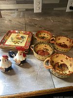 Photo of all ceramic kitchenware items including plates, bowls, and rooster salt and pepper shakers arranged on a countertop.