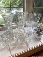 Lot of 5 crystal vases and 3 crystal baskets arranged on windowsill showing overall shapes and cut patterns.