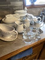 Full set view on countertop showing all white ceramic pieces including duck and rabbit lidded dishes, rabbit teapot, creamer, sugar bowl, and clear glass rabbit dish.