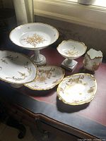 Full view of six white and gold china pieces arranged on desk by window