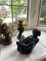Photo showing the two fairy candle holders with stained glass wings alongside the resin boy with dog sculpture on a tiled surface near a window.
