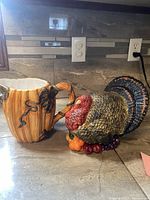 Photo showing two ceramic items on kitchen counter: a pumpkin-shaped pitcher and a turkey-shaped serving dish.