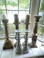 Front view of all six candle holders arranged by height near window with candles on some holders