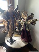 Photo of three tall angel statues on a round table near a window showing full height and different poses