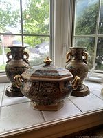 Front view of the set with two matching vases and lidded dish placed on a window sill.