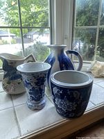 Four ceramic pieces on white tiled window ledge: Fitz & Floyd pitcher with bird, blue gradient pitcher, blue and white floral vase, blue and white ceramic planter.