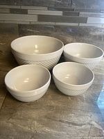 Four white ceramic nesting mixing bowls with textured honeycomb exterior, some utensil wear visible inside largest bowl