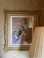 Large framed print of classical sketch showing woman holding a child in an ornate gold-tone frame with a lamp partially blocking view