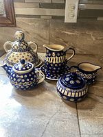 Photo of all five ceramic pieces arranged on a countertop including the cheese lady, teapot, pitcher with plate, creamer, and lidded sugar dish.