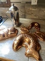 Photo showing all five vintage copper molds with animal and object shapes along with a glass and stainless steel French coffee press.