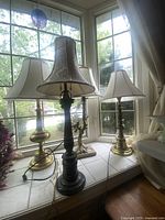 Five vintage lamps arranged on tiled window ledge, showing various bases and shades with natural light from window.