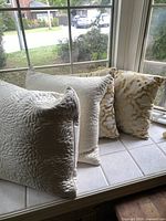 Set of 6 decorative pillows displayed on a tiled window ledge, showing three white quilted pillows with floral pattern and three gold and white damask-pattern pillows.