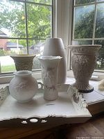 Wide shot of all six cream vases and the cream decorative tray on a white surface by a window showing overall condition and style.