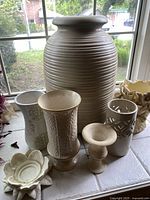 Front view of seven cream-colored home decor pieces arranged on a tiled surface by a window showing details of each item