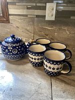 Teapot with four matching mugs, arranged on a countertop showing overall set condition and patterns.
