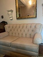 Front view of the vintage cream fabric couch showing tufted back and rolled arms under gold-framed mirror.