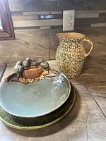 Three ceramic pieces including the Robinson Ransbottom green spongeware pitcher and two plates, one with bird decoration and one solid green plate.