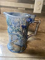 Side angle of Wade Heath blue pottery pitcher showing rabbit detail at base and bird on handle.