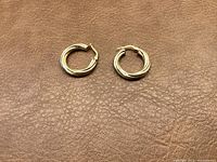 Pair of gold hoop earrings laid flat on brown leather background