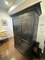 Front angled view of black wooden armoire with double doors, showing panel design and round knobs.