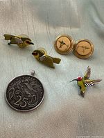 Photo showing pair of bird-shaped earrings, hummingbird brooch, round bird pendant, and a 25-cent coin for size reference