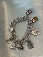 Full view of the silver double chain link charm bracelet with multiple varied charms attached, laid flat on a surface.