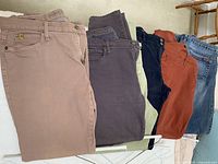 Top view of five pairs of folded denim jeans in various colors laid out together.