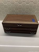 Front view of the brown wooden jewelry box showing two drawers with silver handles and decorative gold border around the top.