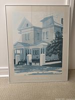 Framed print showing a blue-toned illustration of a traditional house with porch, pillars, and surrounding greenery.