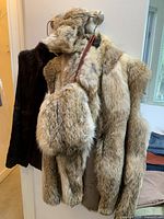 Photo showing medium size fur vests including a dark brown vest, and a light brown/cream vest with matching muff and headband fur accessories