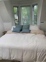 Full frontal view of the king bed made with bedding, showing mattress and pillows against windows.