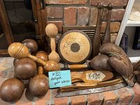 Overall photo showing the entire antique sports equipment lot including wooden dumbbells, leather boxing gloves, a weight disc, and a wooden paddle.