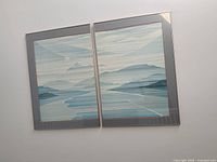 Photo of two framed mountain range art prints side by side, colors blue and gray, modern metallic frames.