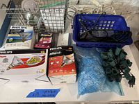 Photo showing various Philips branded halogen and EcoVantage bulbs in original packaging along with DuraMax bulbs. Also includes string light sockets with plug, remote control and some power cords in a blue basket.