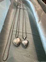 Two sterling silver heart pendant necklaces laid out, showing chain and pendant sizes and designs.