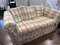 Front and side view of multicolor plaid fabric love seat on wooden floor demonstrating overall condition and style.